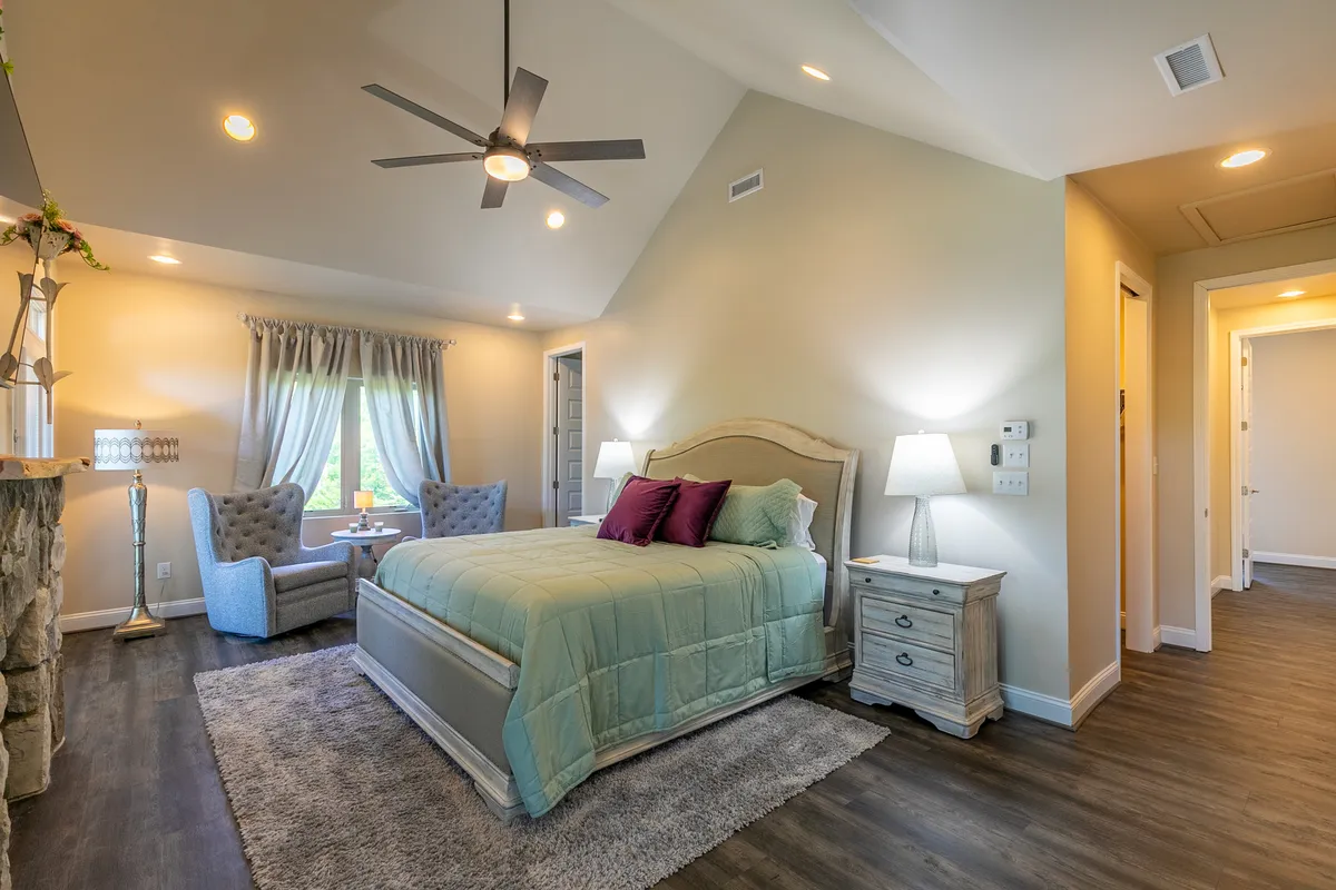 A cozy bedroom featuring a large, inviting bed with plush armchairs positioned near the window. Natural light filters into the serene space, and a decorative lamp and patterned rug add warmth and comfort, creating a peaceful retreat perfect for winding down with a pet after a day of adventure.