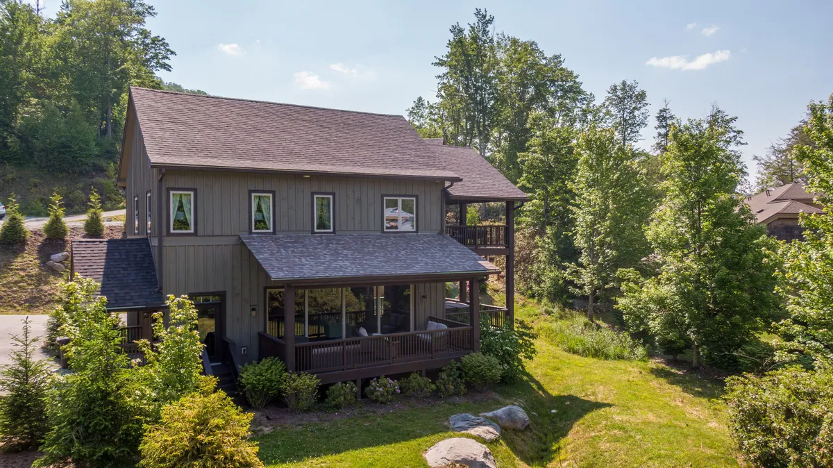 The house is shown surrounded by abundant greenery, with an inviting porch area that beckons relaxation. The composition includes the structure's architecture, hinting at home comforts paired with the seclusion of the natural landscape.