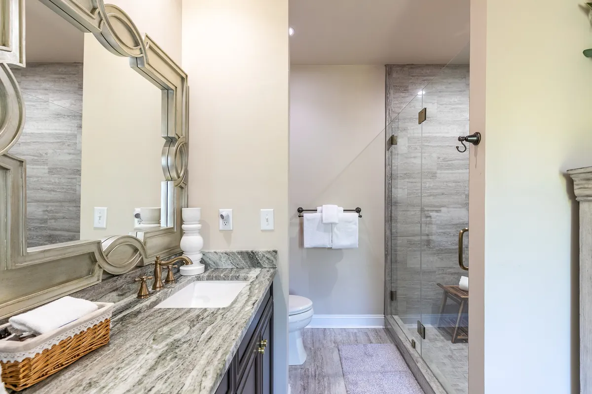 A tranquil bathroom featuring a large decorative mirror, sleek granite countertop, and a glass-enclosed shower. Soft lighting and upscale finishes evoke a spa-like ambiance.
